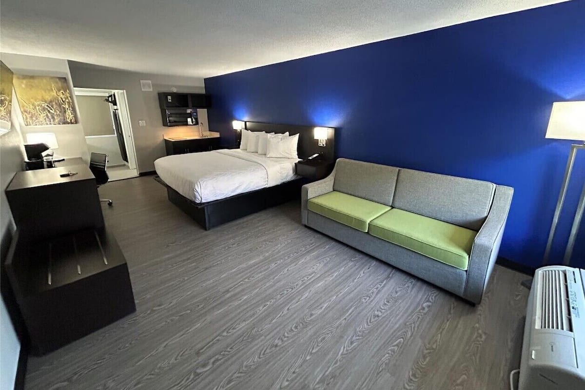 A hotel room with a bed, a sofa, a desk, and a wall-mounted TV.