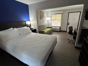 A hotel room with a large bed, a desk, a chair, a sofa, and a window.