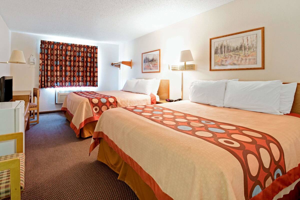 A hotel room with two beds, a desk, and a chair.