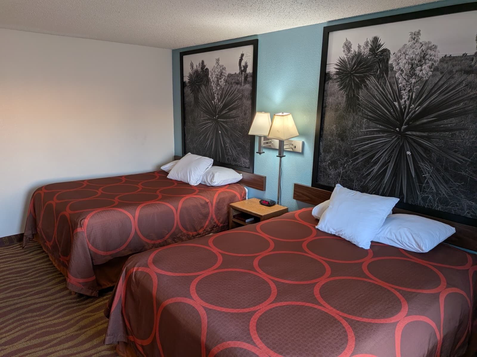 Une chambre d’hôtel avec deux lits, une table de chevet, une lampe et des œuvres d’art murales.