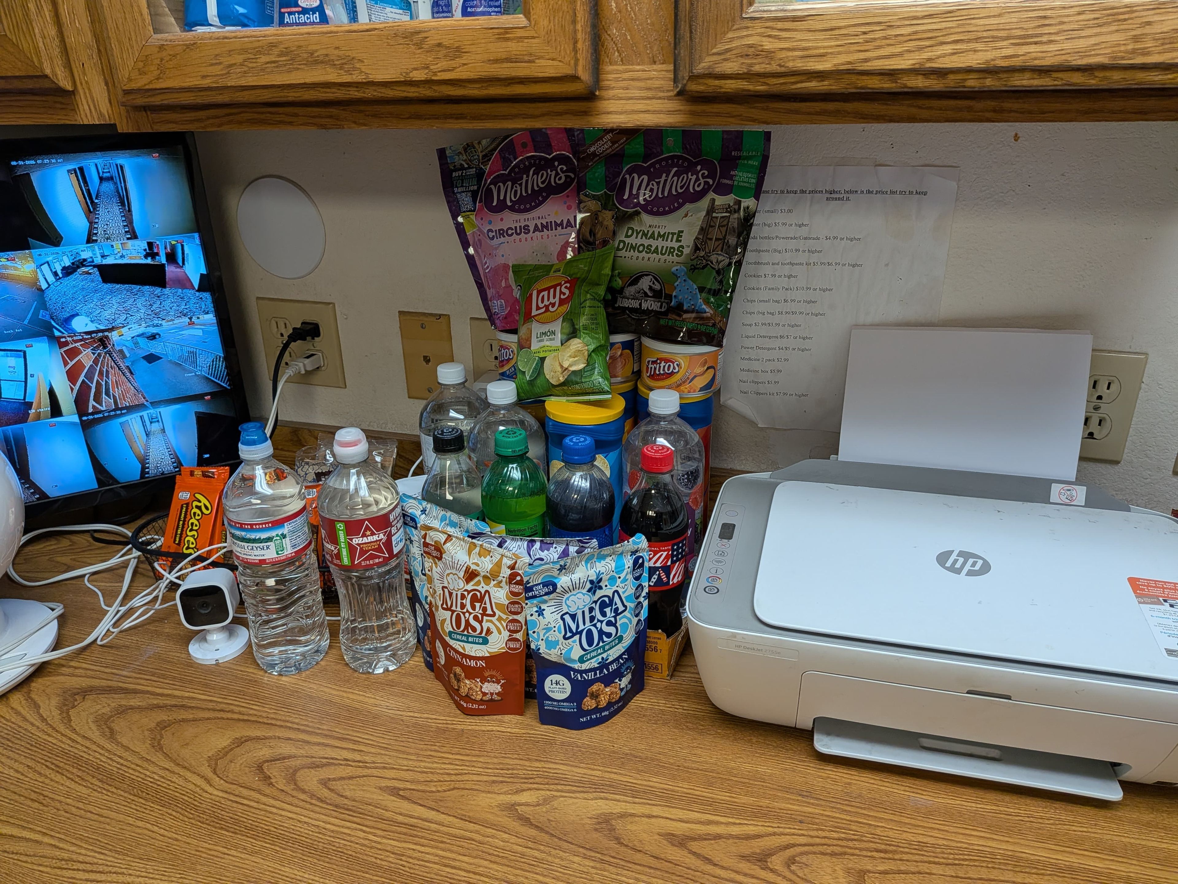 Un bureau avec un écran d’ordinateur affichant les images d’une caméra de surveillance, une imprimante et divers articles alimentaires et boissons.