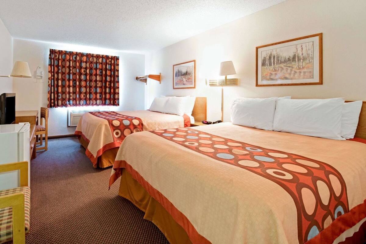 A hotel room with two beds, a desk, a chair, a TV, and two wall-mounted lamps.