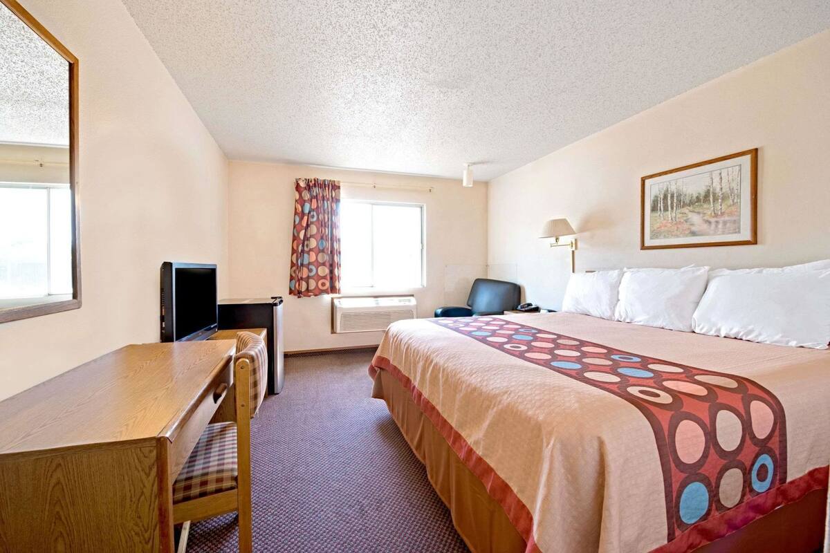 A hotel room with a bed, desk, chair, television, and a window with curtains.