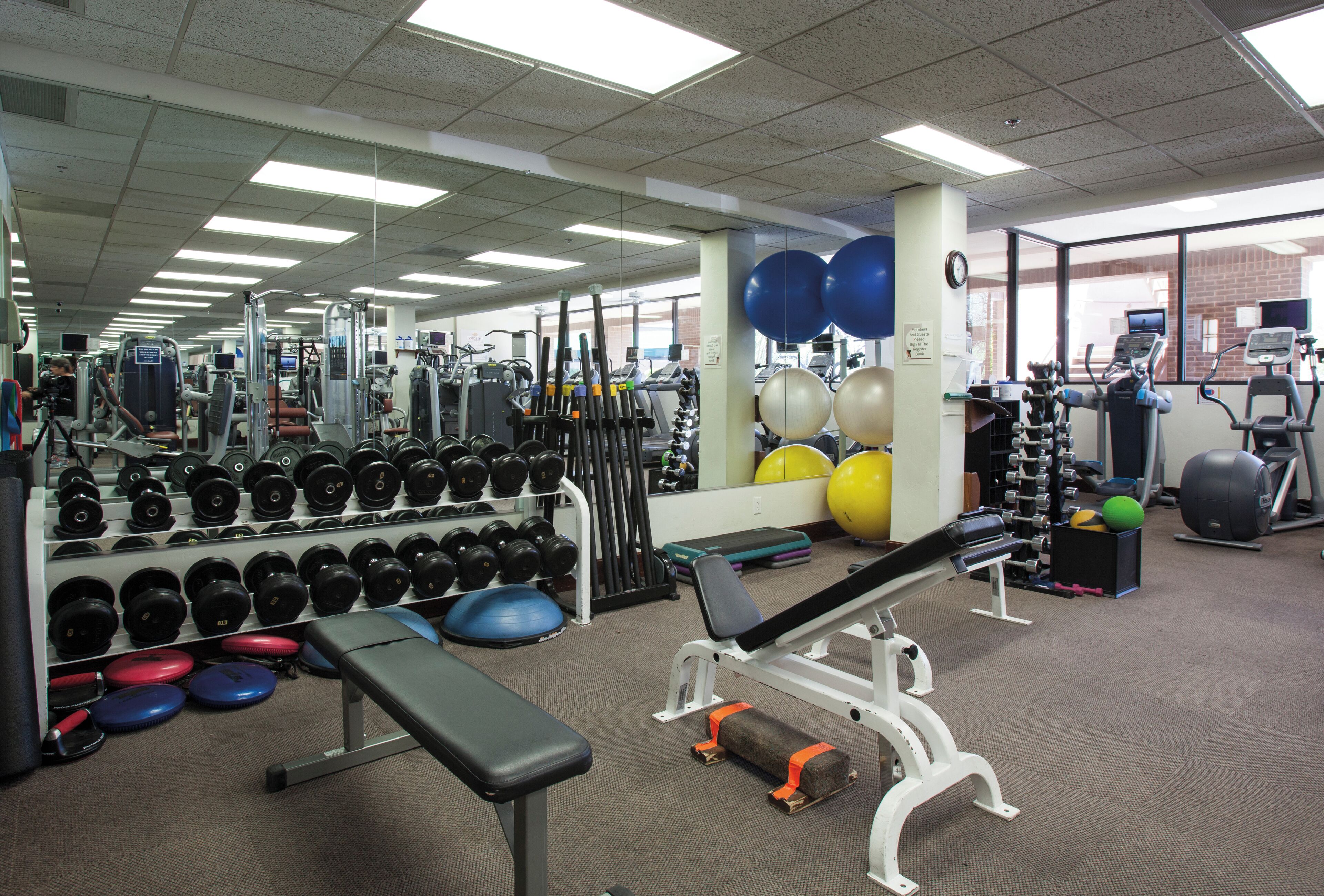 Un gimnasio con diferentes equipos de ejercicio, como mancuernas, bancos y cintas de correr.