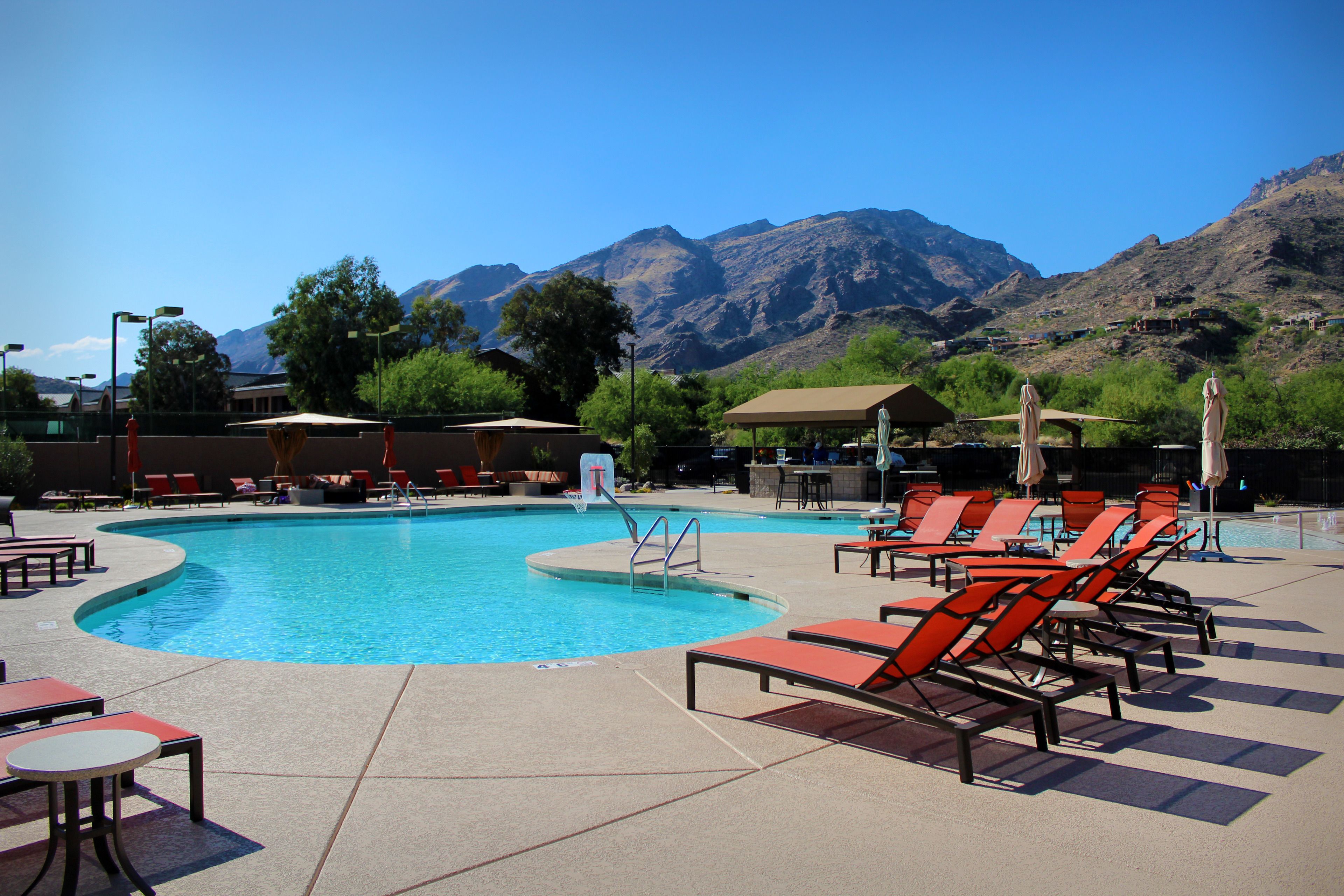 A pool area with lounge chairs and tables, surrounded by mountains.