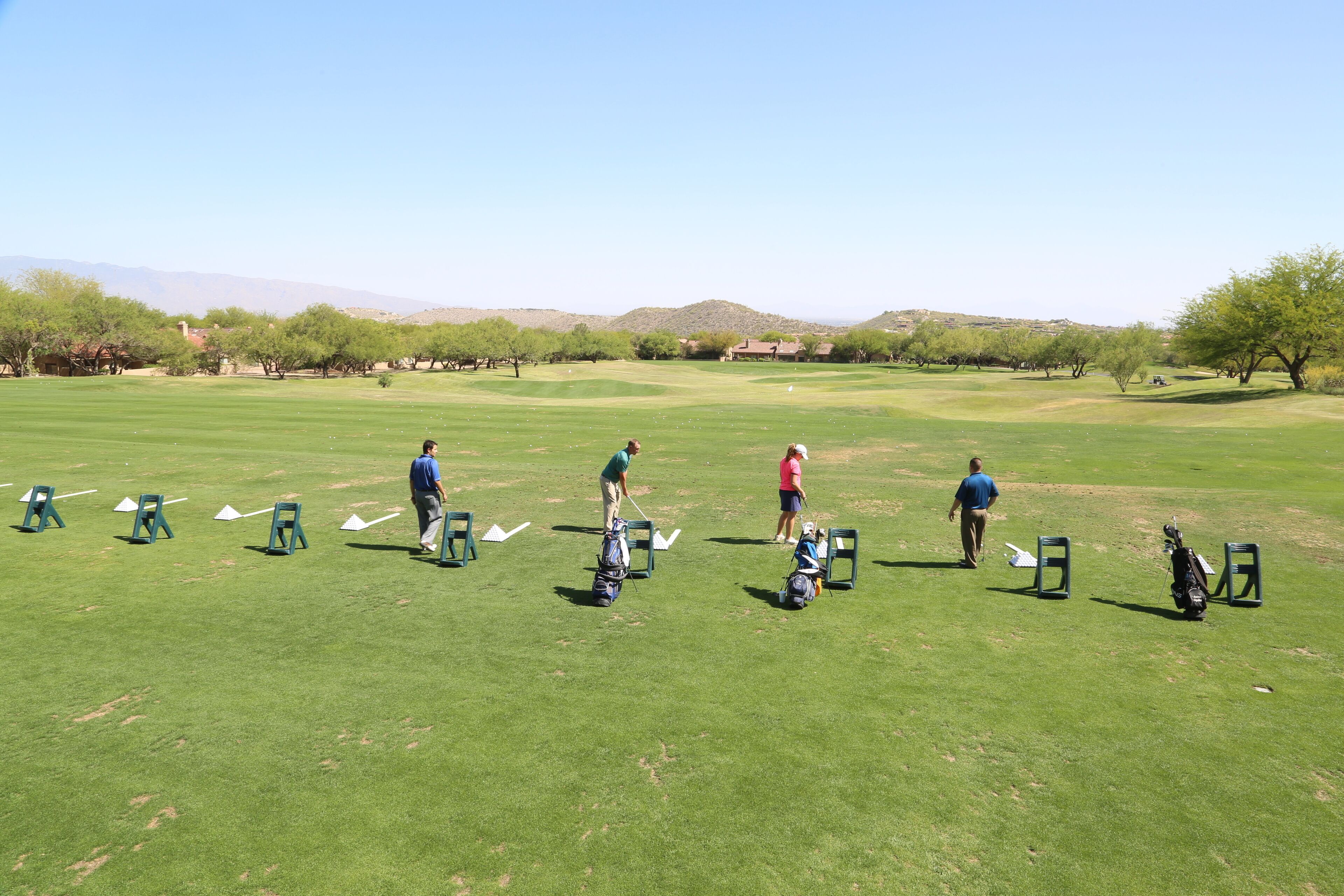 Un campo de golf con múltiples plataformas de salida, cielo despejado y montañas a lo lejos.