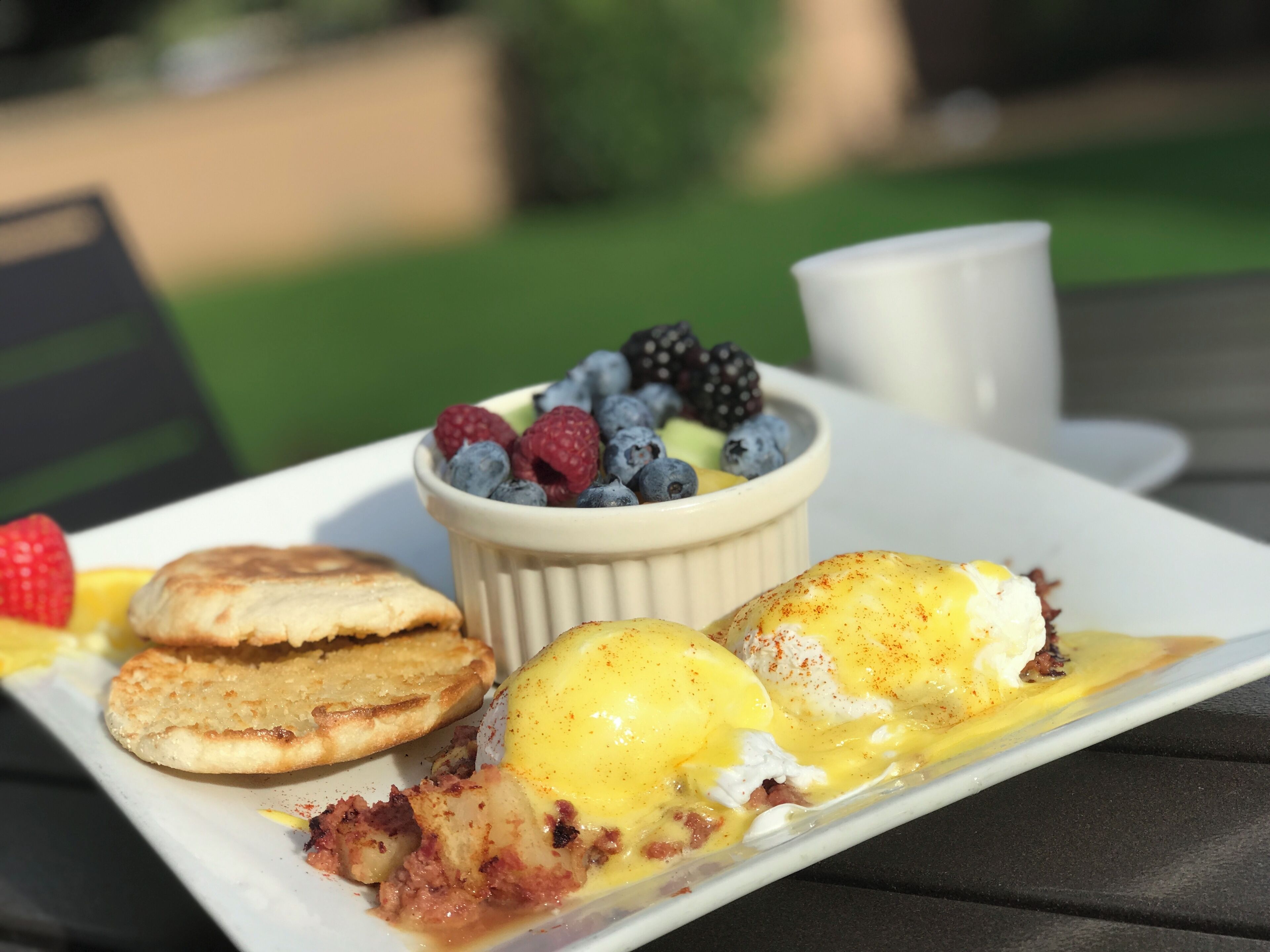 A breakfast plate with eggs benedict, berries, and pancakes.