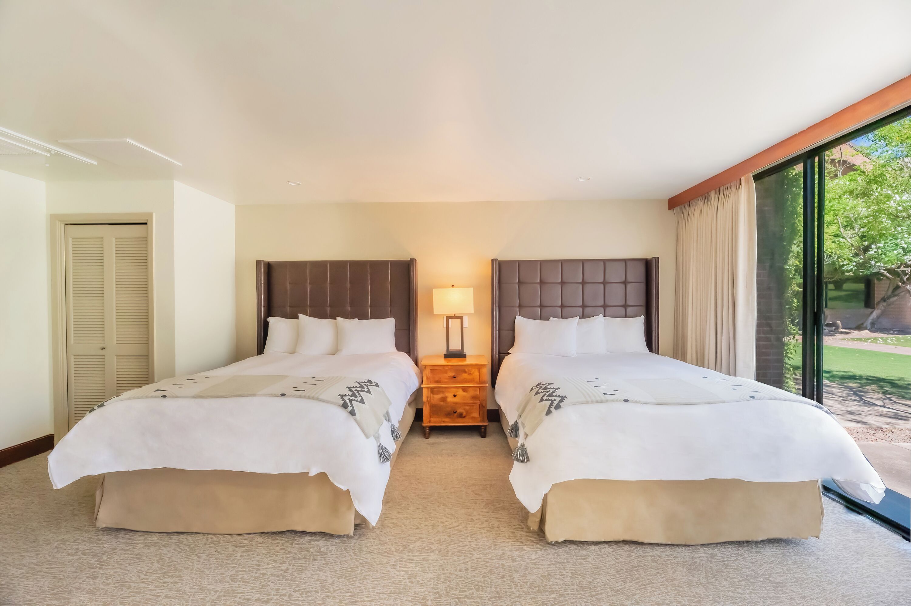 Une chambre d’hôtel avec deux lits, une table de chevet avec une lampe et une grande fenêtre donnant sur l’extérieur.