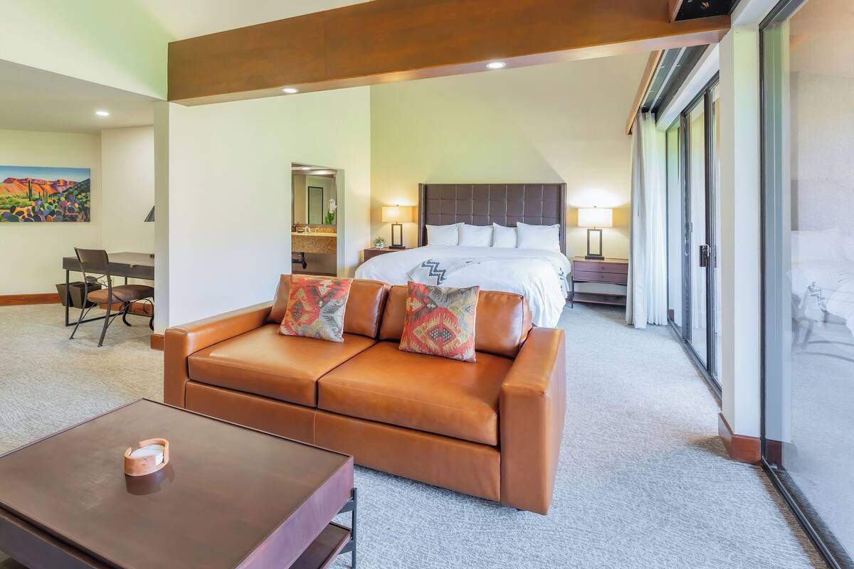 Ein Hotelzimmer mit einem großen Bett, einem braunen Ledersofa, einem Holztisch und einem Bild an der Wand.