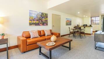 A living room with a brown leather sofa, a wooden coffee table, and a dining area with a table and chairs.