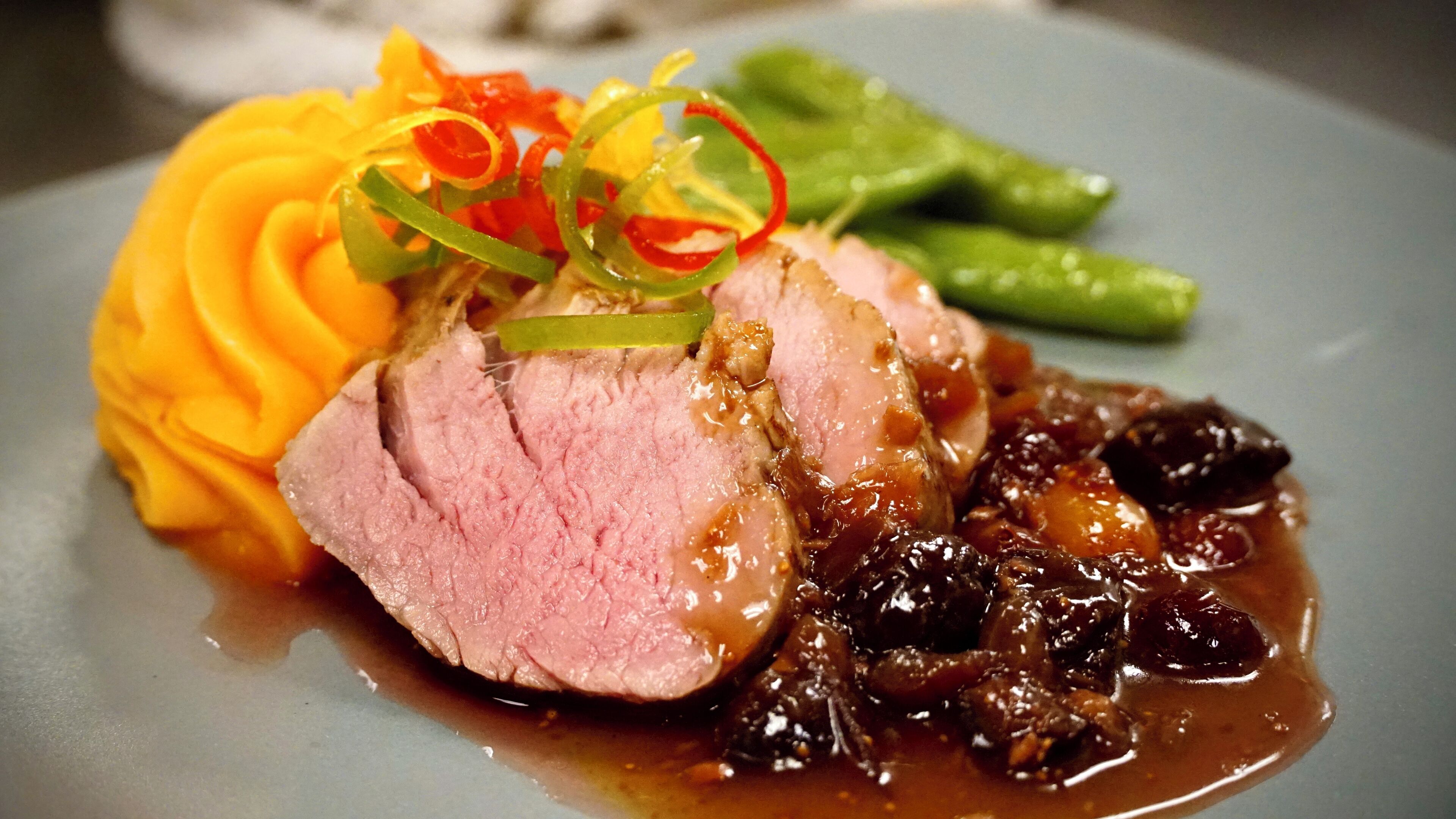 A plate with sliced meat, a side of mashed potatoes, and a dark sauce.