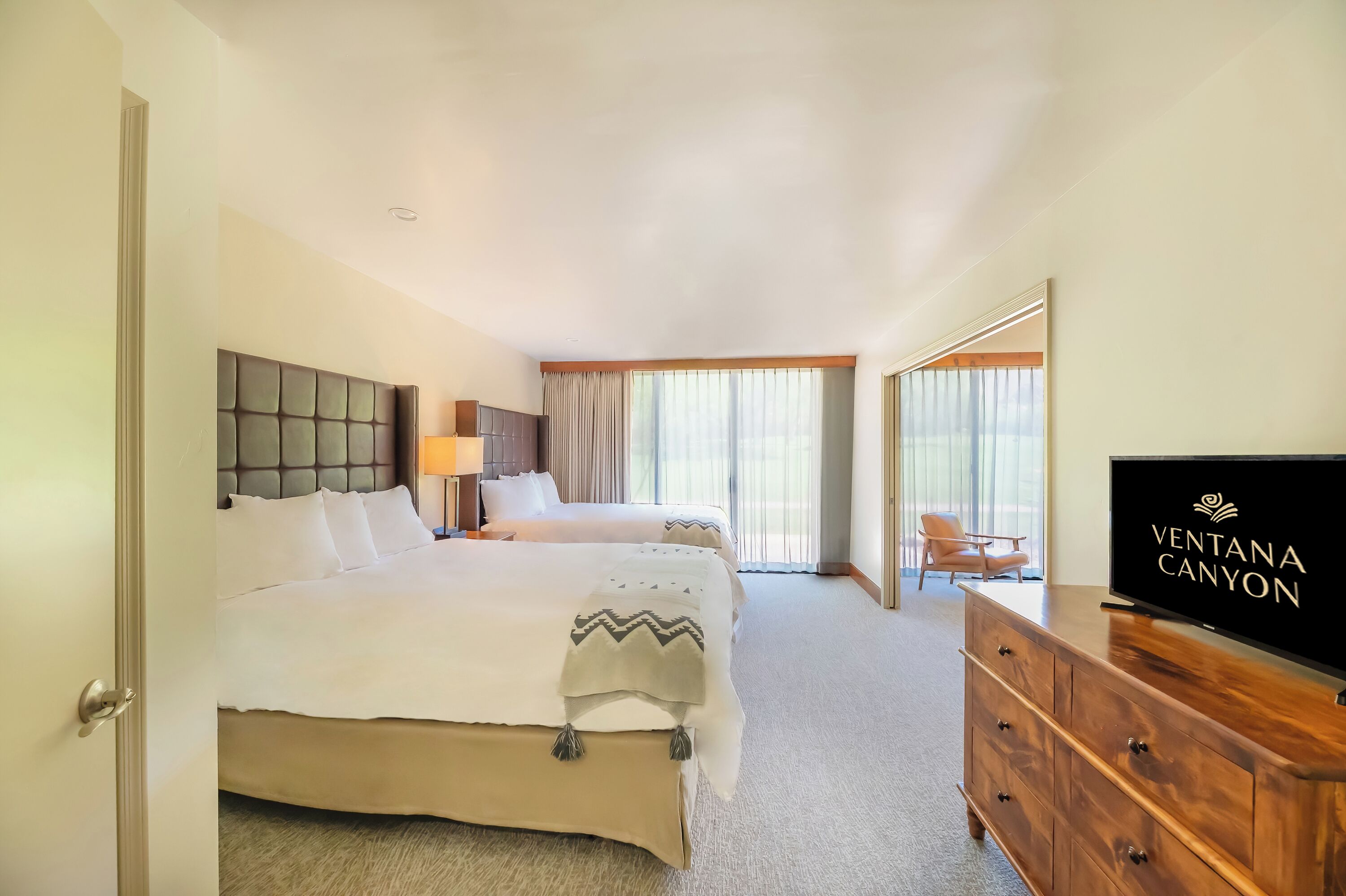 A hotel room with a large bed, a television, and a view of the outside through the window.