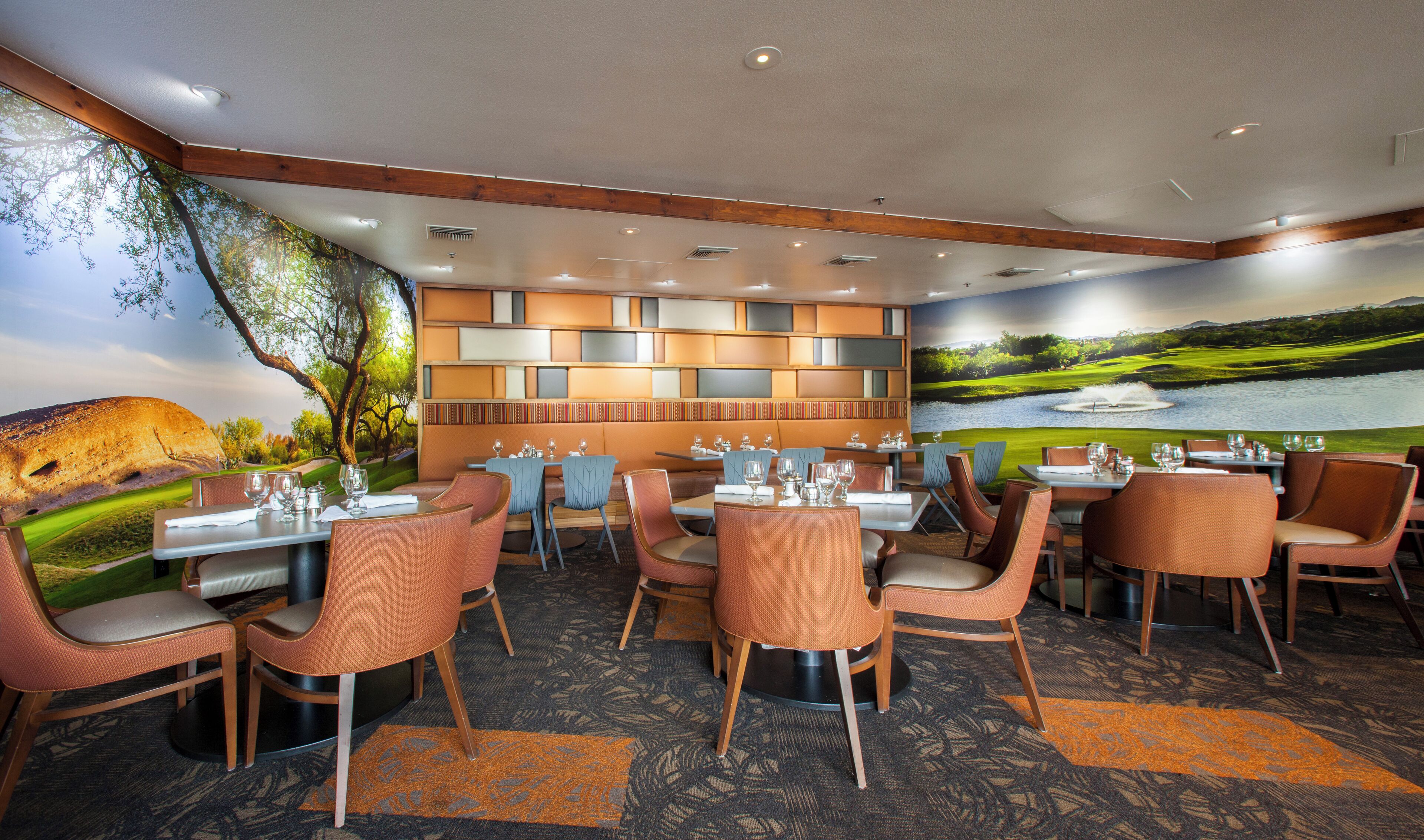 A restaurant with a view of a golf course and a lake. Tables are set with glasses and cutlery.