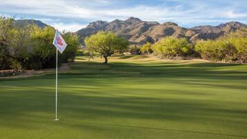 Un campo de golf con una bandera, árboles y montañas al fondo.