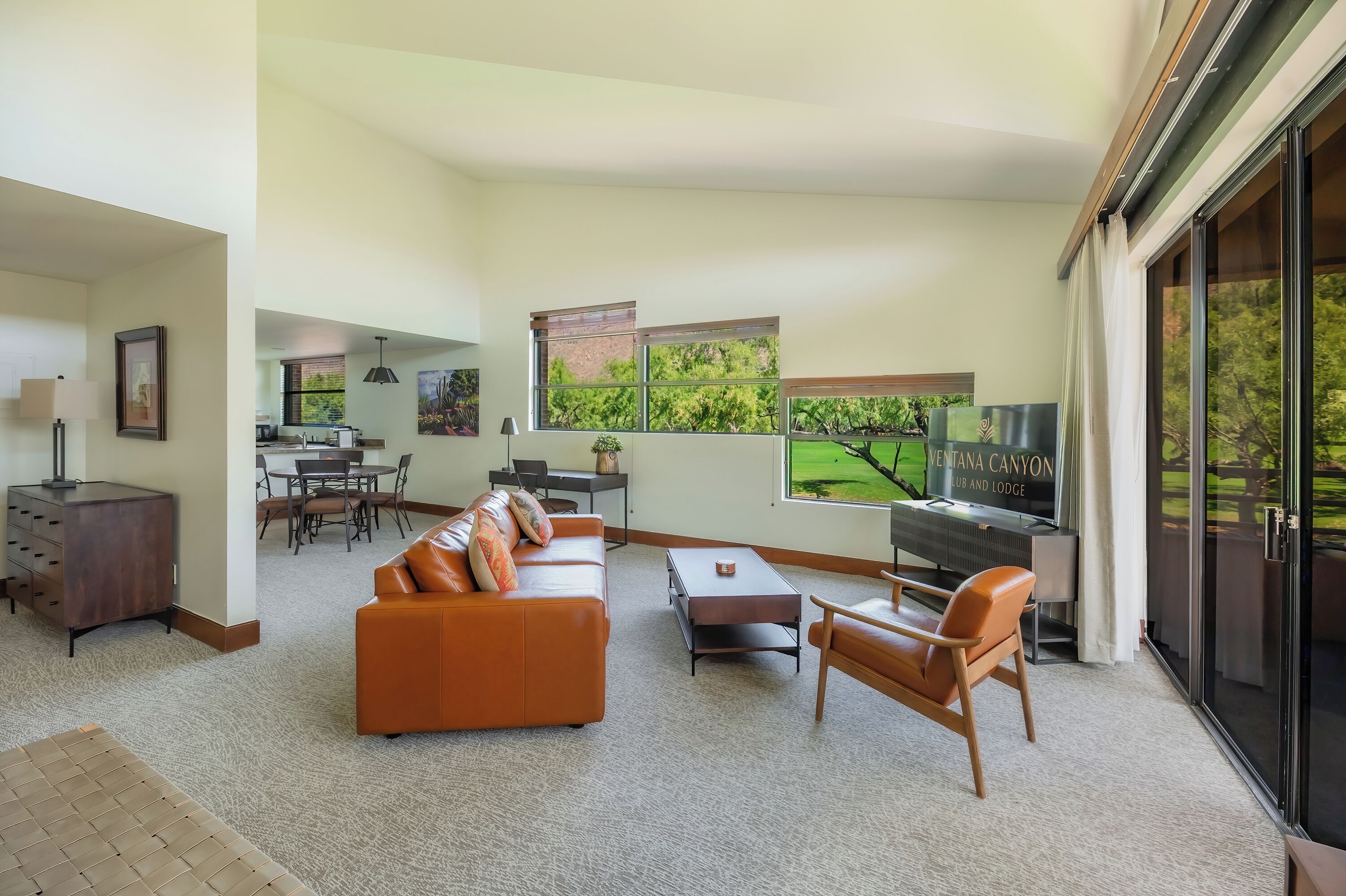 A spacious living room with a large orange sofa, a piano, and a dining area in the background.