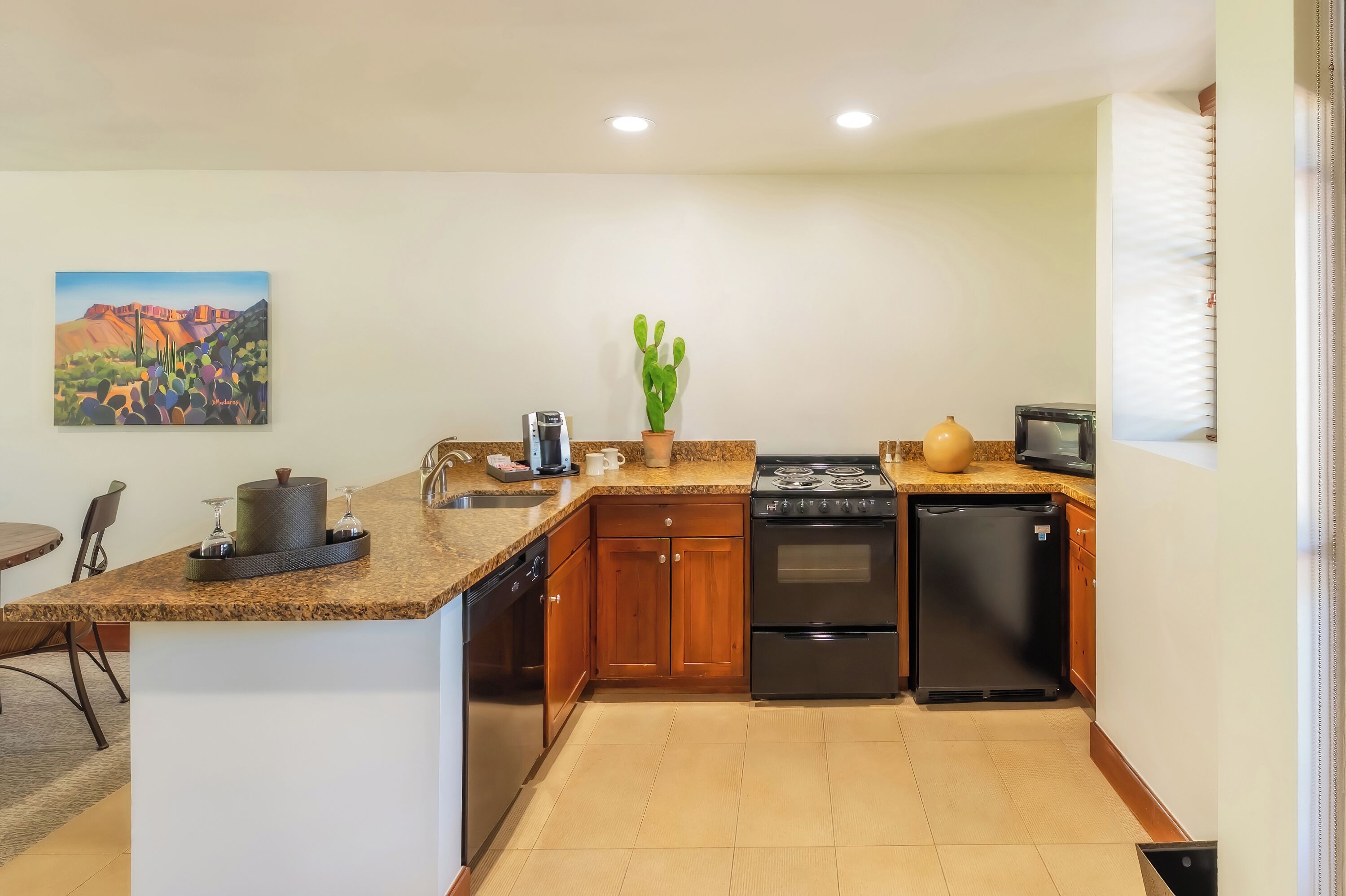 A compact kitchen with granite countertops, wooden cabinets, a stove, refrigerator, and a coffee maker.
