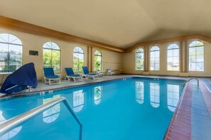 An indoor swimming pool with clear glass windows, blue lounge chairs, and a pool lift sign.