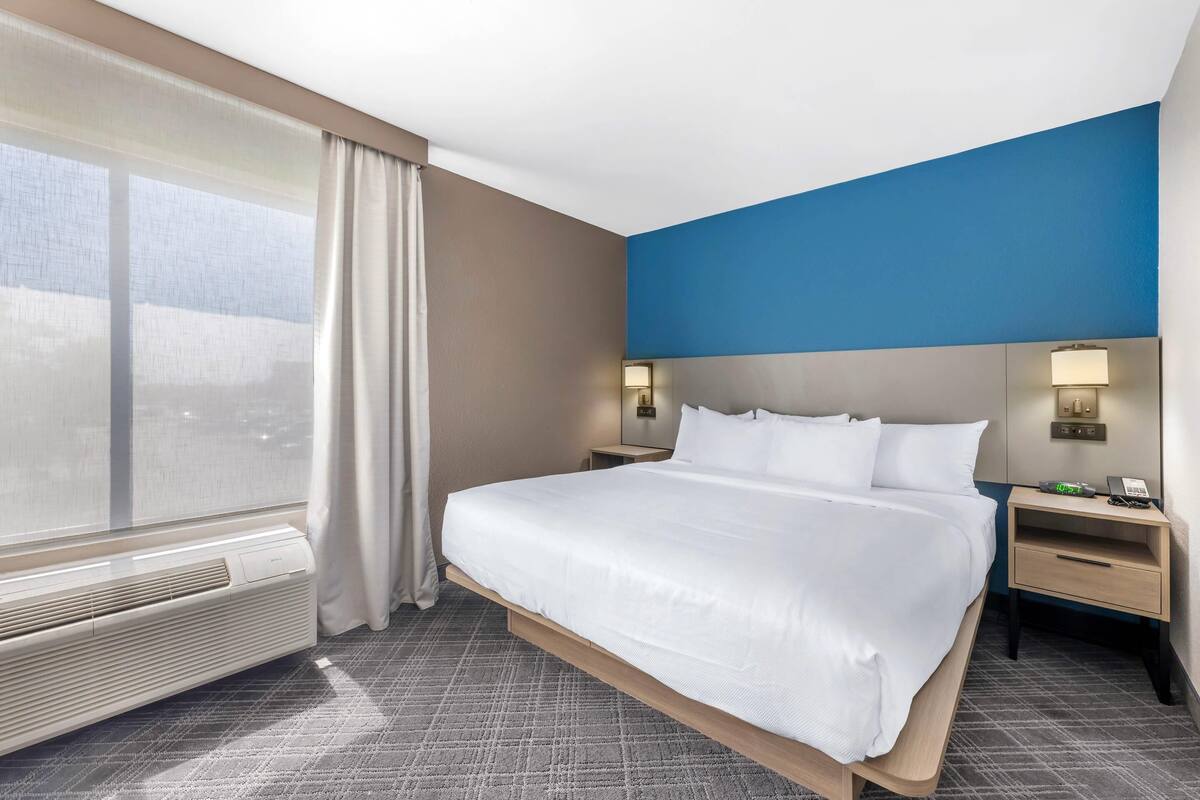 Een hotelkamer met een groot bed, twee nachtkastjes, een raam met gordijnen en een wandlamp.