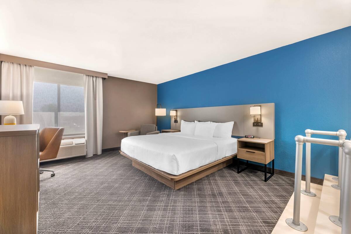Een hotelkamer met een groot bed, een bureau, een stoel, een nachtkastje en een raam met gordijnen.