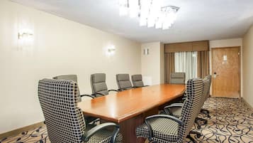 Un salón de conferencias con una mesa de madera y sillas estampadas, una araña y una puerta con cortinas.
