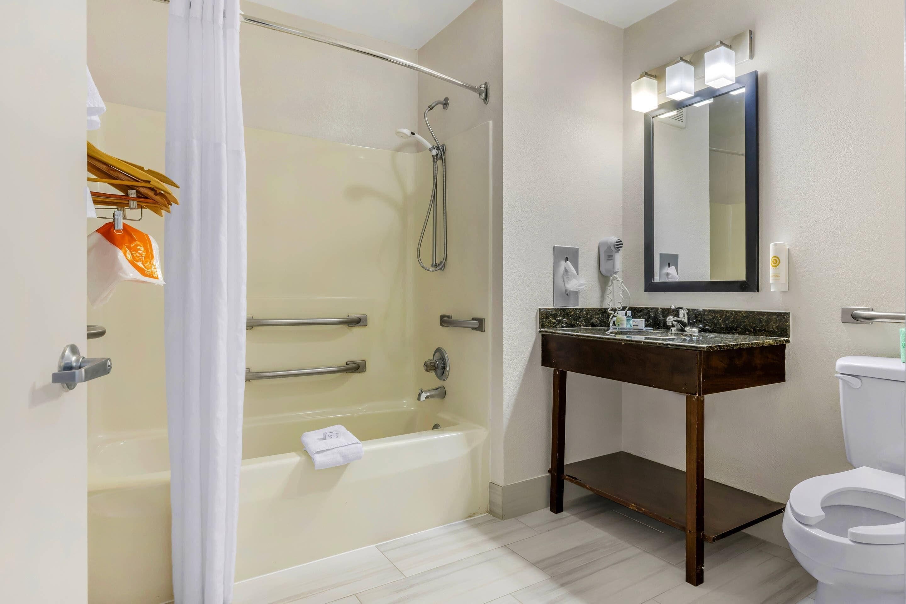 A bathroom with a bathtub, shower, vanity with a mirror, and a toilet.