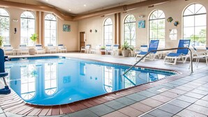 An indoor swimming pool with clear water, surrounded by lounge chairs and potted plants.