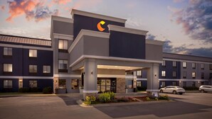 A modern hotel with a prominent logo on the facade, a covered entrance, and a parking area.