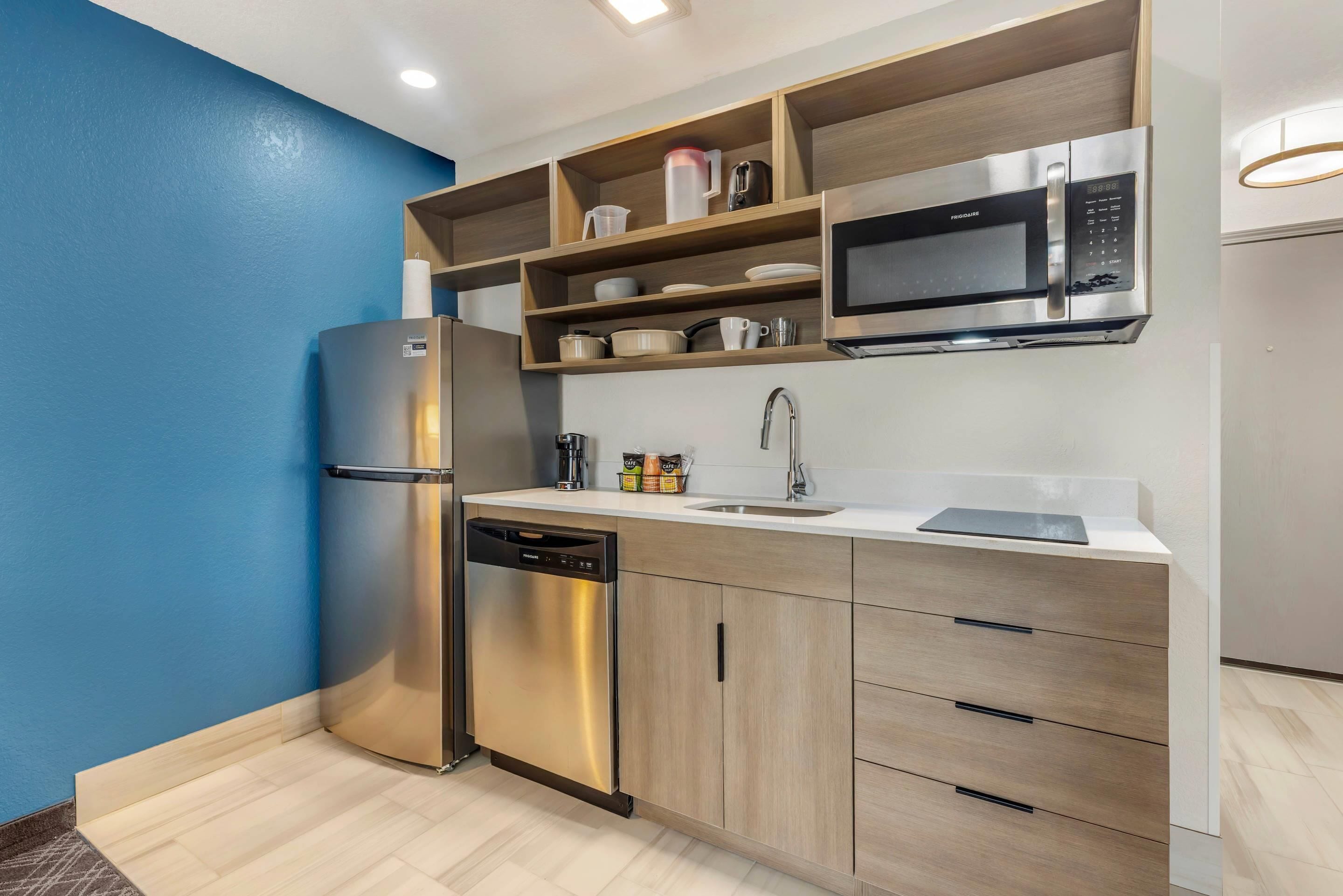 A modern kitchen with a stainless steel refrigerator, built-in microwave, and wooden shelves.