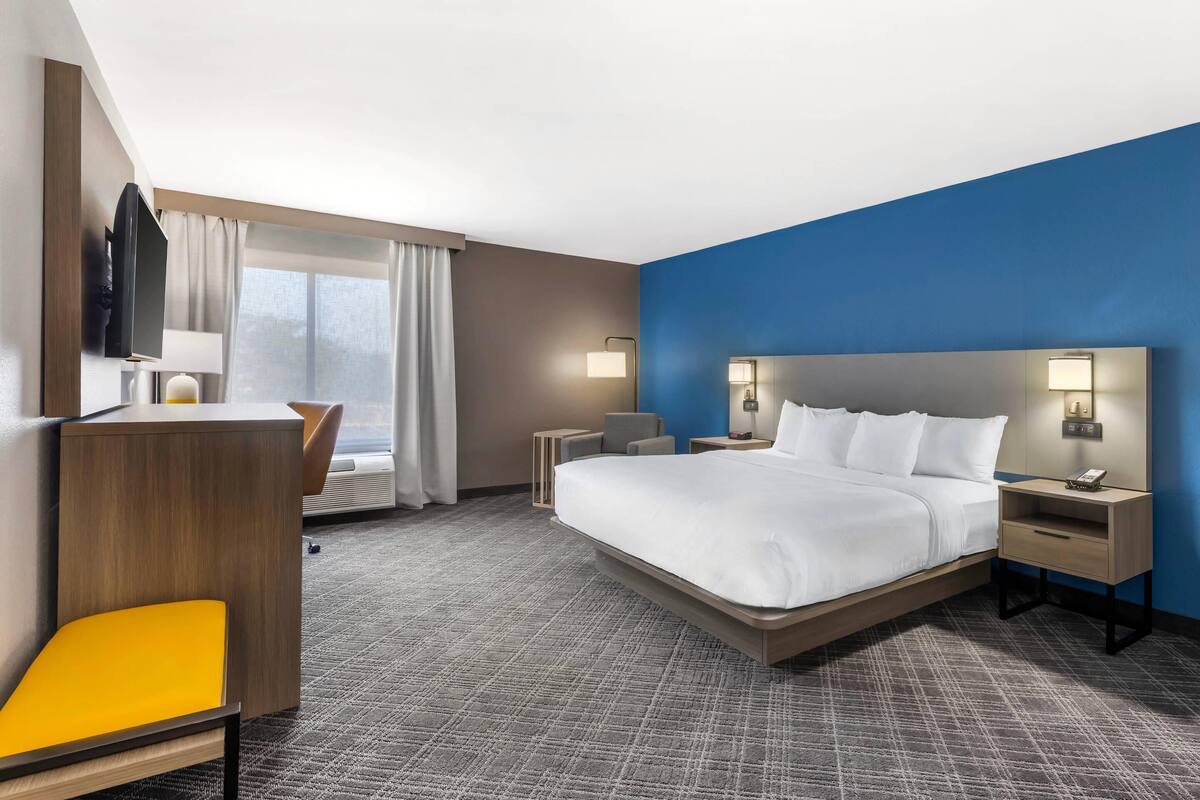 Een moderne hotelkamer met een groot bed, een bureau met stoel, een flatscreen televisie en een raam met gordijnen.