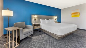 A hotel room with a large bed, a nightstand, a lamp, a chair, and a small table.