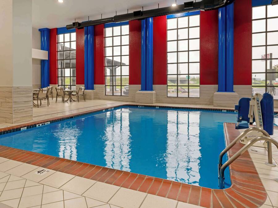 Ein Schwimmbecken mit Fliesen umrandet, mit blauen und roten Vorhängen und Blick durch große Fenster ins Freie.