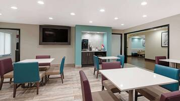 A modern dining area with tables and chairs, a kitchen area, and a flat-screen TV mounted on the wall.
