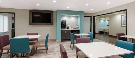 Un espace repas moderne avec des tables et des chaises, un coin cuisine et un téléviseur à écran plat fixé au mur.