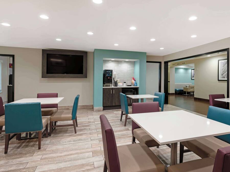 A modern dining area with tables and chairs, a kitchen area, and a flat-screen TV mounted on the wall.