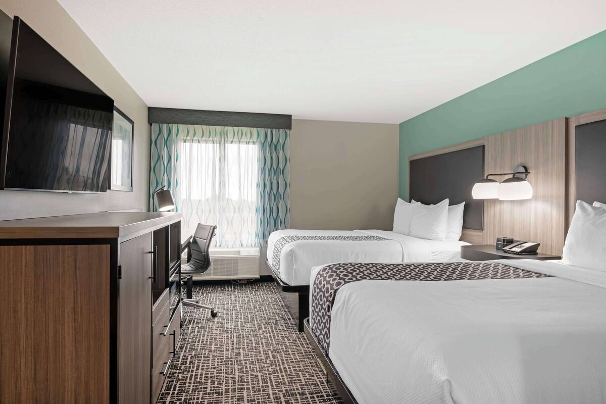 A hotel room with two beds, a desk with a flat-screen TV, a chair, a desk lamp, and a telephone.