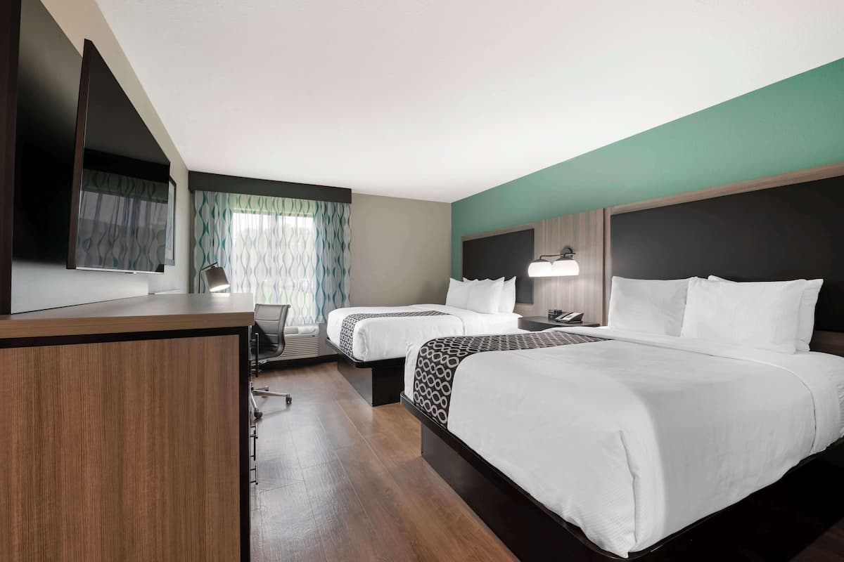A hotel room with two beds, a desk, a chair, a TV, and a window with curtains.