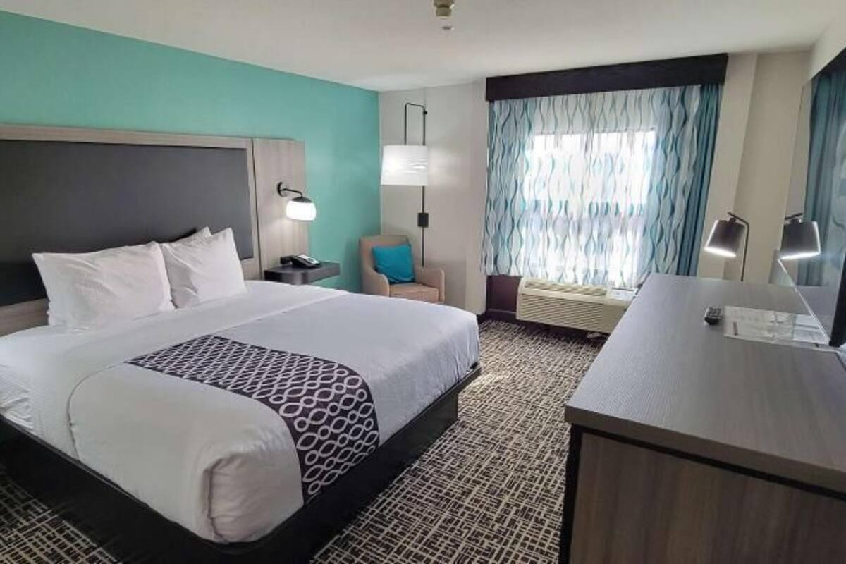 A hotel room with a large bed, bedside tables, a desk, a chair, a TV, and a window with curtains.