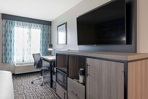 Habitación de hotel con cama, escritorio con silla, televisor y minibar.