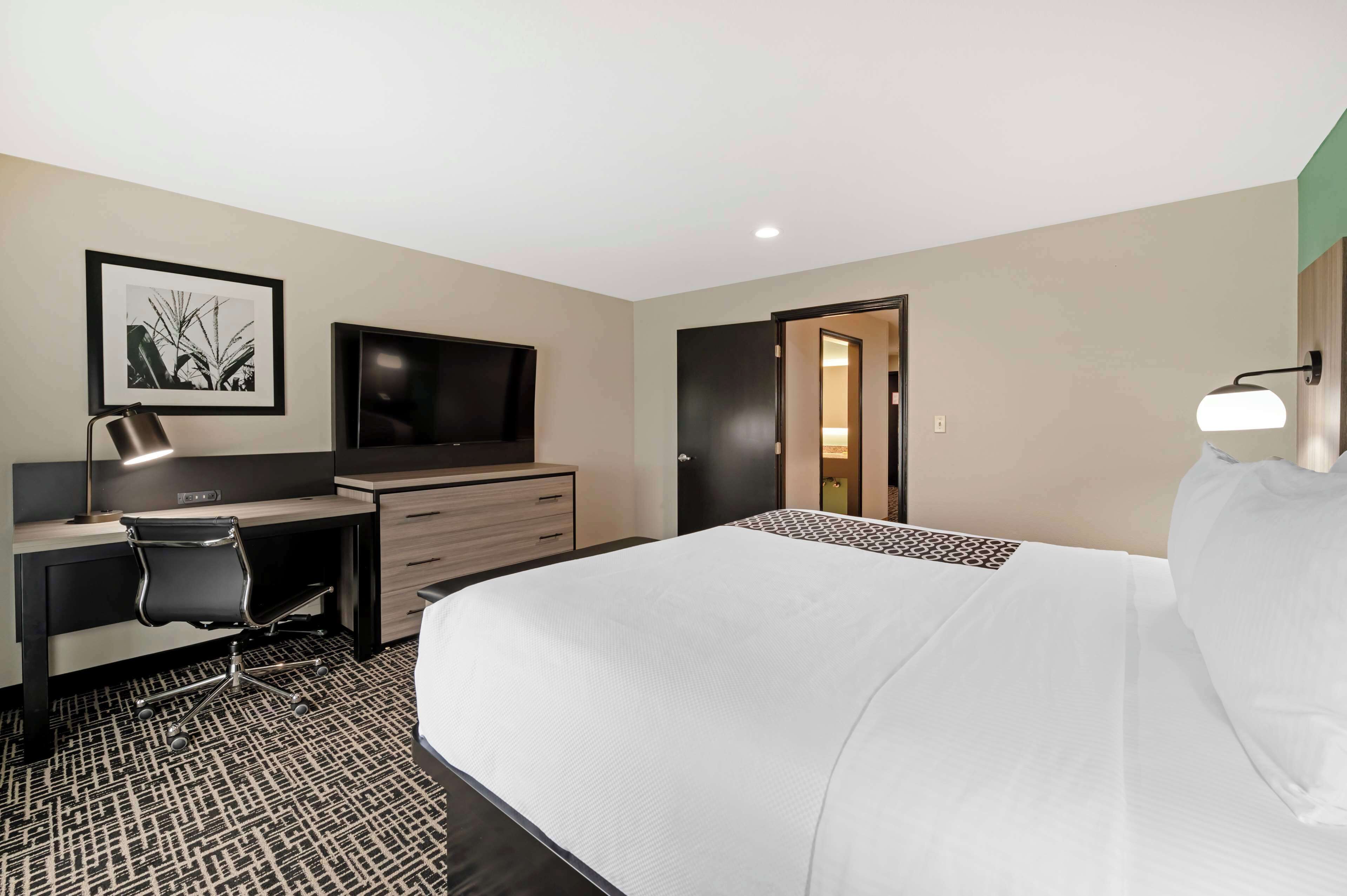 Ein Hotelzimmer mit einem großen Bett, einem Schreibtisch mit Stuhl, einem Fernseher und einem gerahmten Bild an der Wand.
