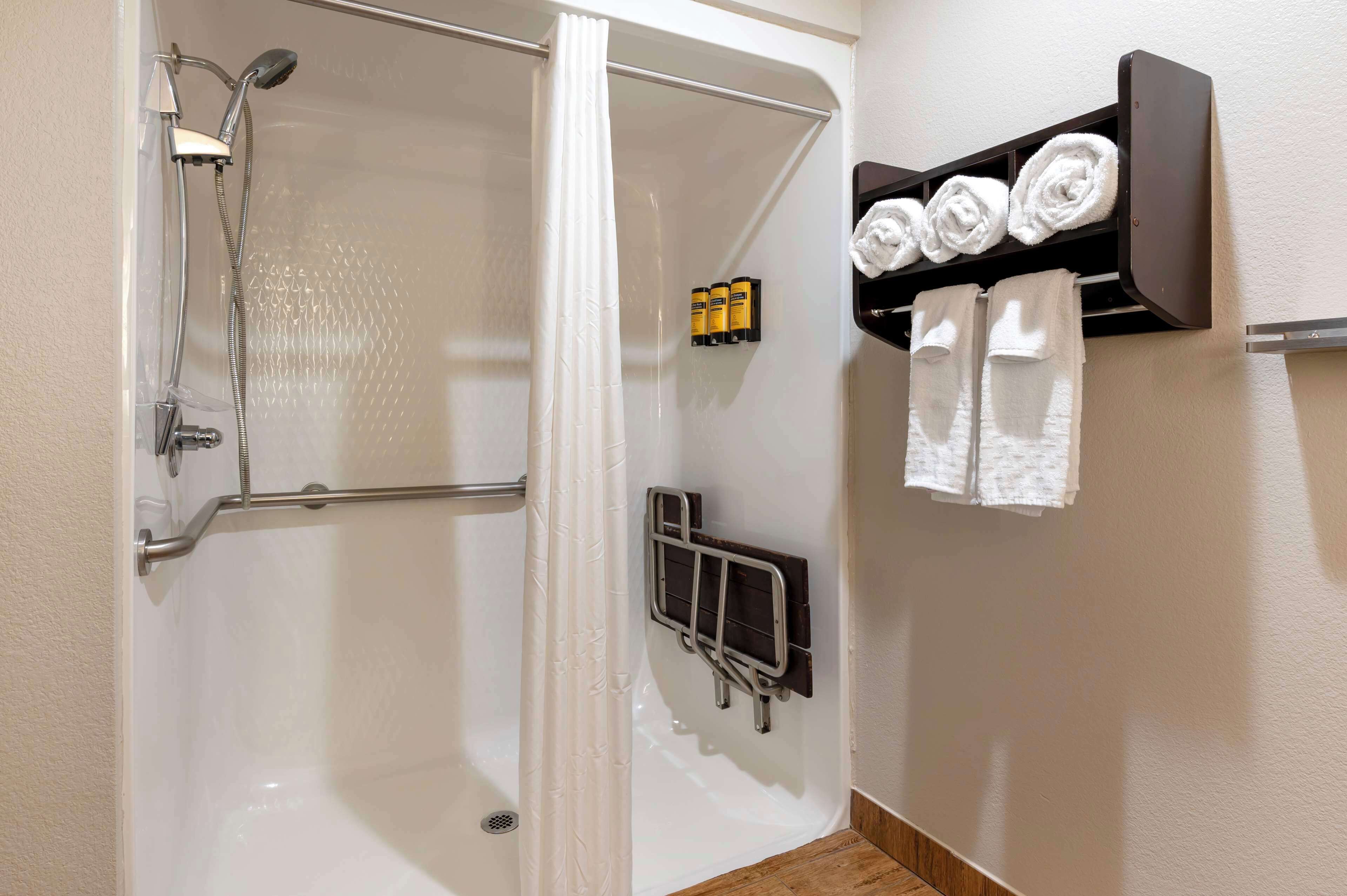 A shower area with a glass door, a handrail, and a towel rack with towels and toiletries.