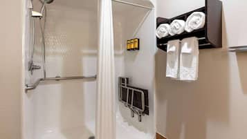 A shower area with a glass door, a handrail, and a towel rack with towels and toiletries.