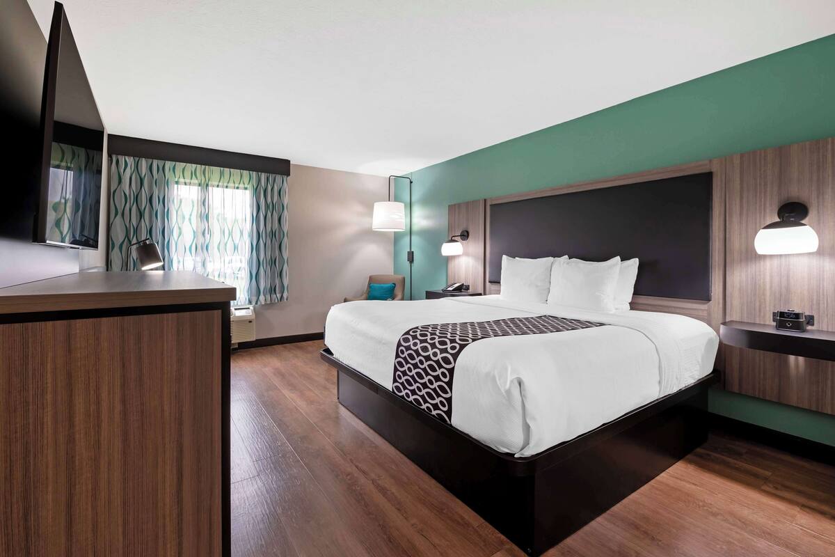 A hotel room with a large bed, a desk, a mirror, and a window with curtains.