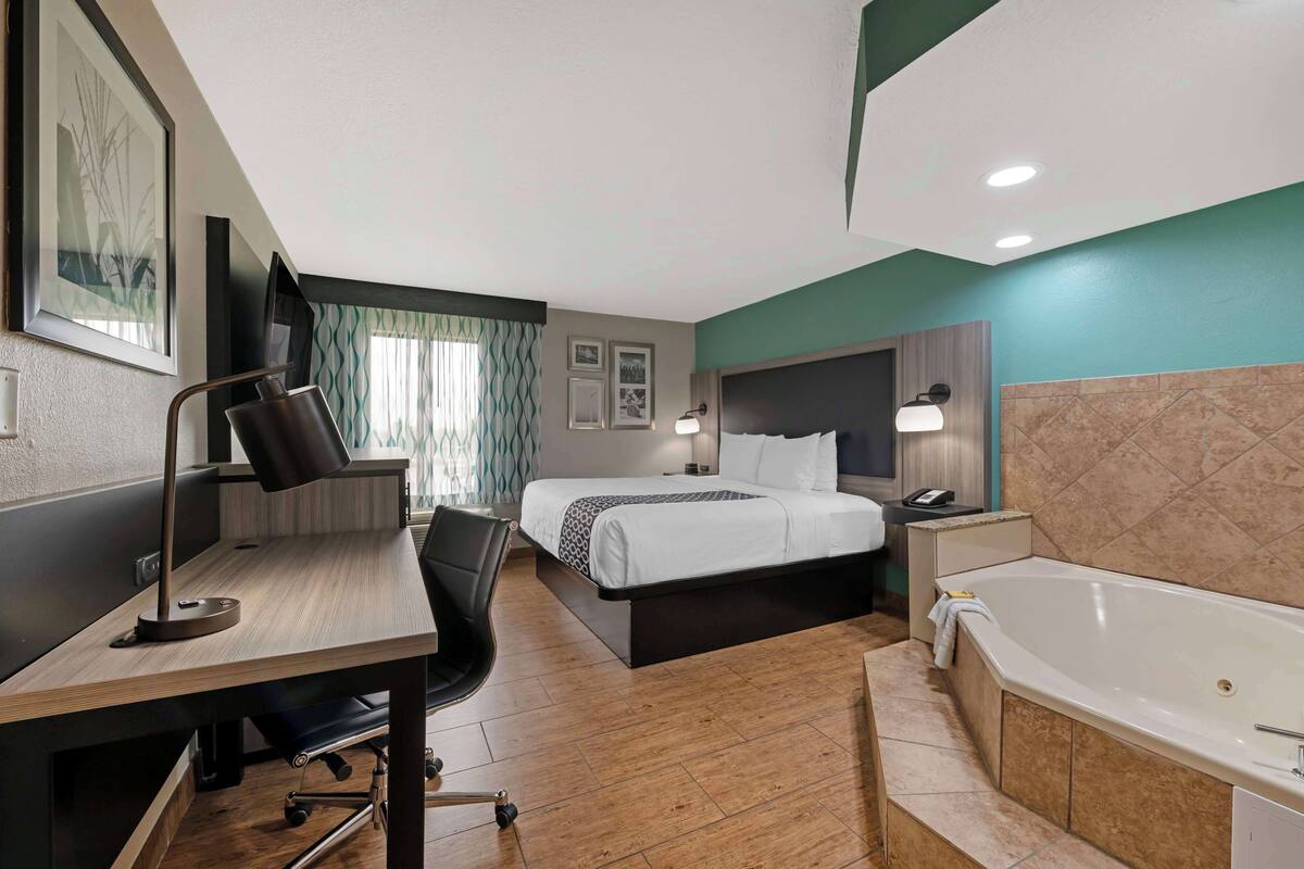 A hotel room with a desk, two beds, a bathtub, and a TV.
