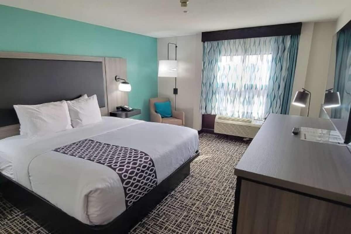 A hotel room with a large bed, bedside tables, a desk, a chair, a TV, and a window with curtains.