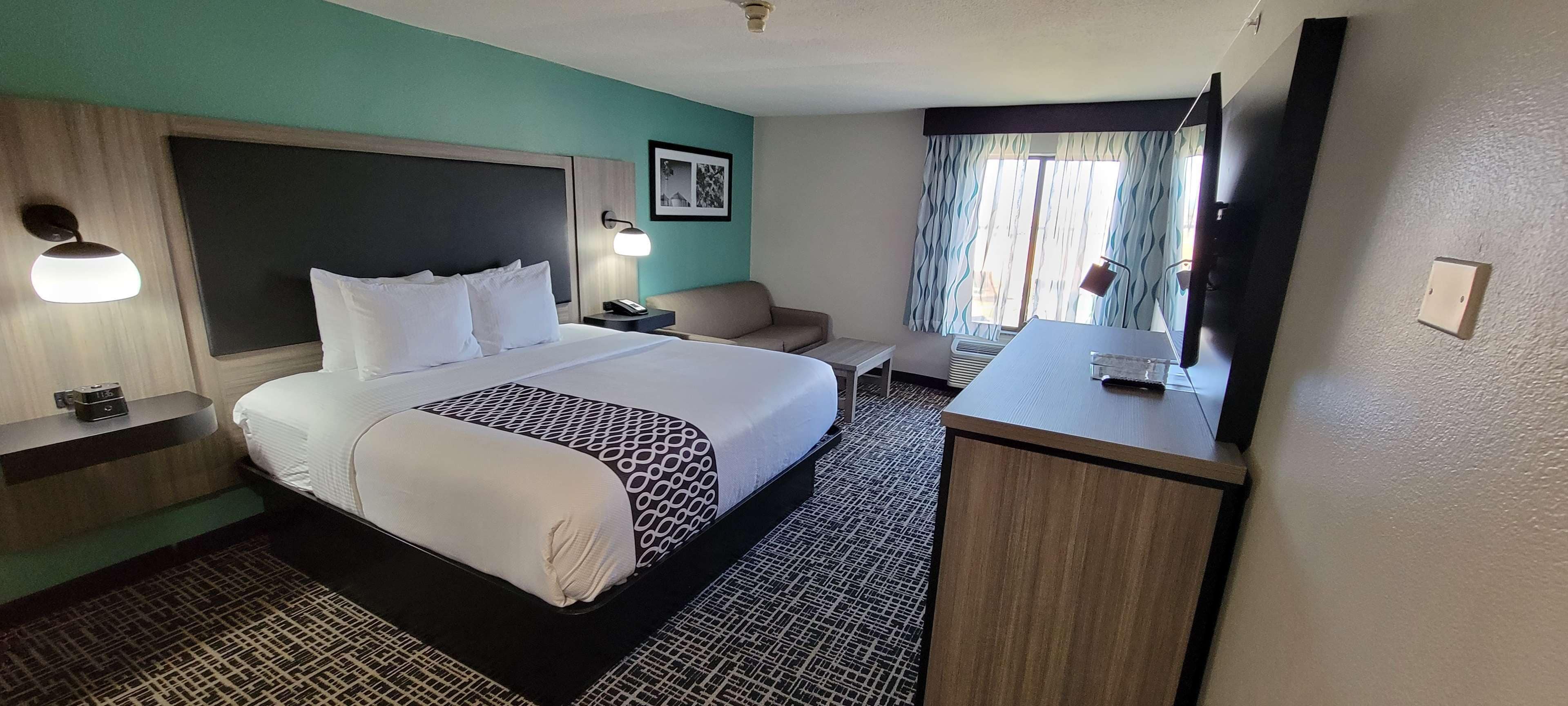 A hotel room with a large bed, bedside tables, a desk, a chair, a television, and a window with curtains.