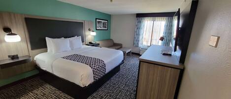 A hotel room with a large bed, bedside tables, a desk, a chair, a television, and a window with curtains.