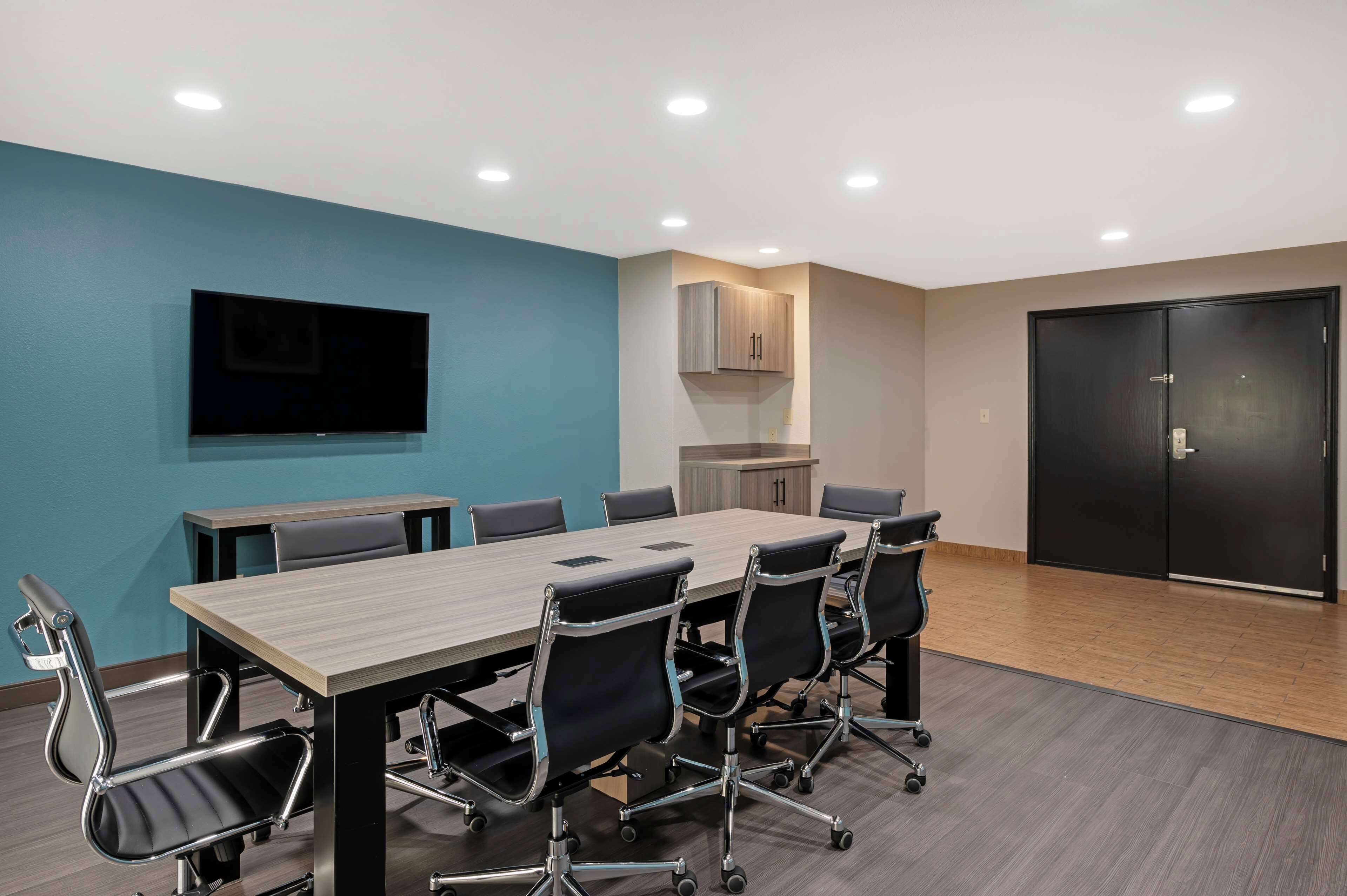 A conference room with a long table, six chairs, a flat-screen TV, cabinets, and a door.