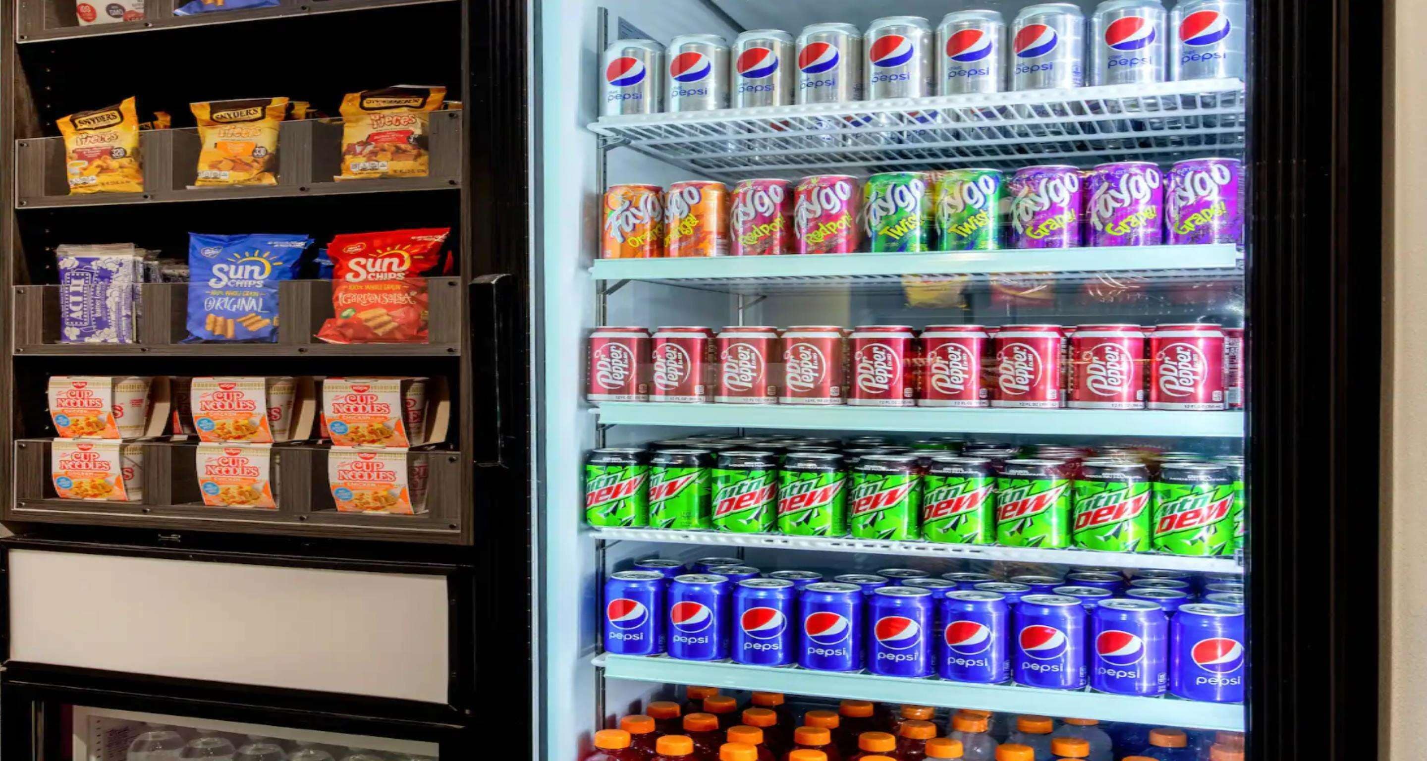 Ein Automaten steht voll mit verschiedenen Snacks und Getränken, darunter Chips, Limonaden und Energydrinks.