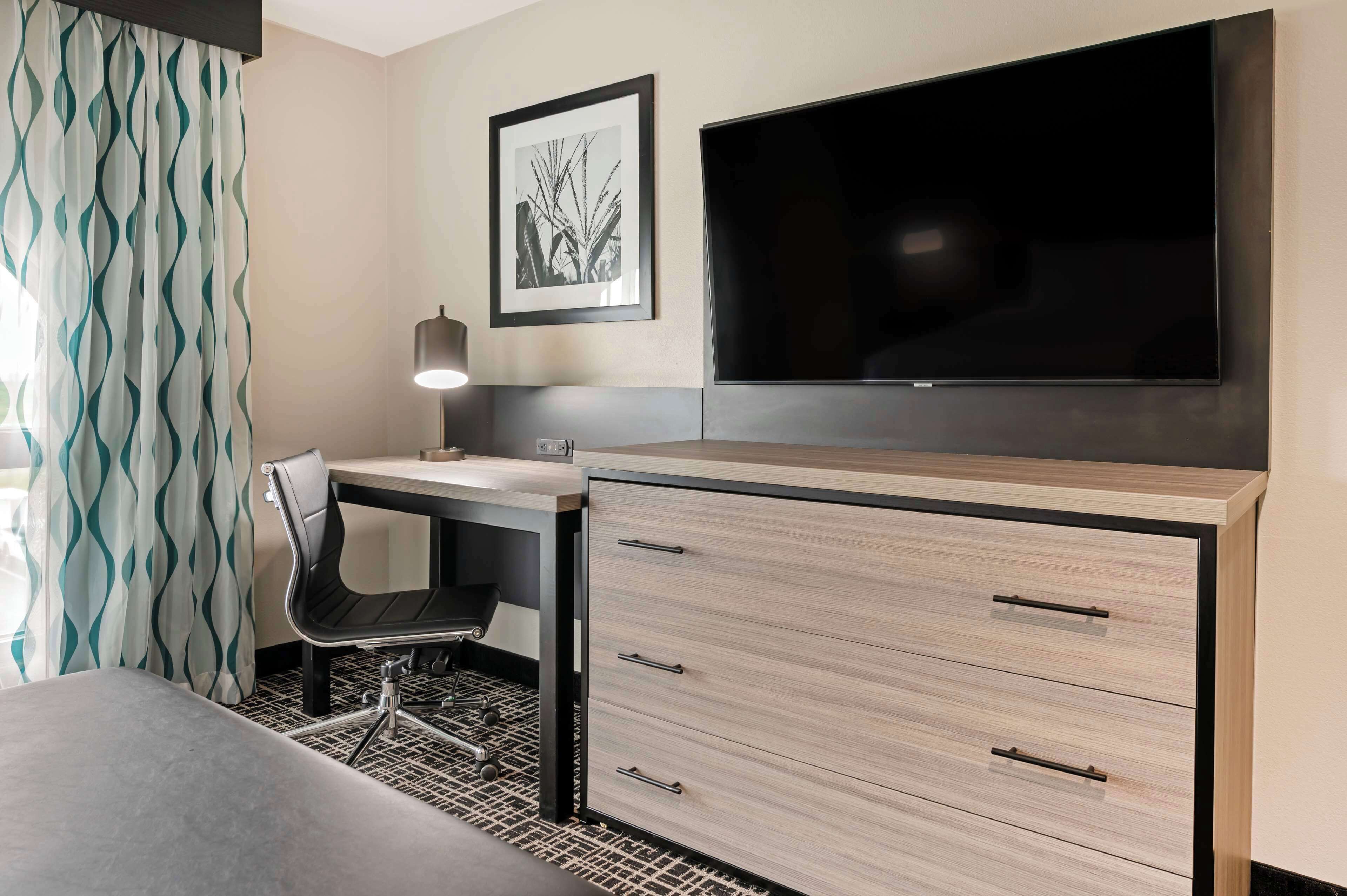 A hotel room with a bed, a desk with a chair, a TV, and a desk lamp.