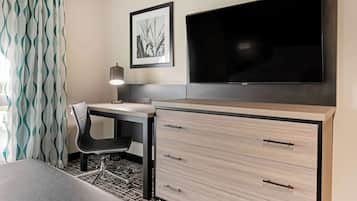 A hotel room with a bed, a desk with a chair, a TV, and a desk lamp.